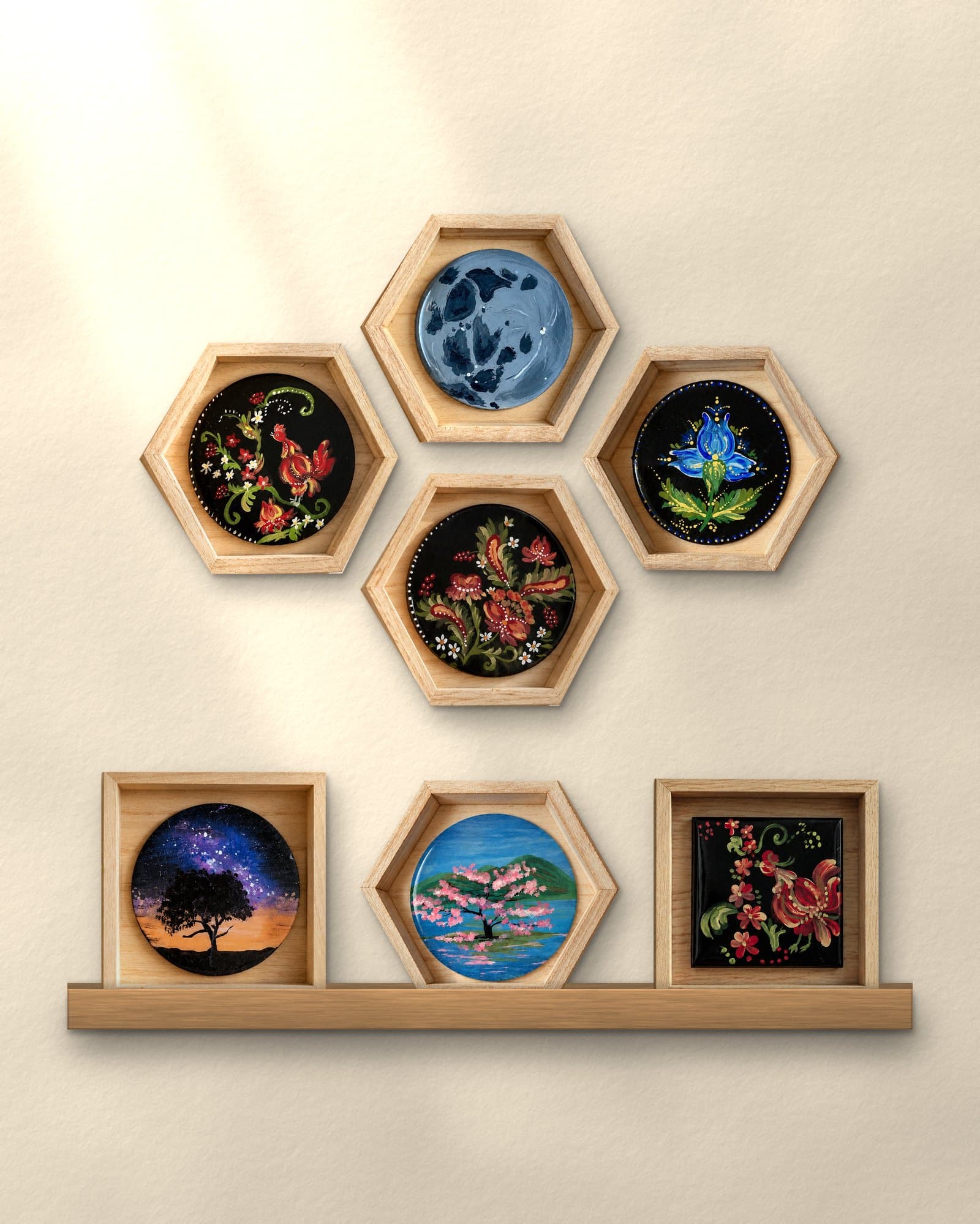 A gallery wall of Yana's hand-painted pieces in hexagon and square wood frames, with three more standing on a picture ledge